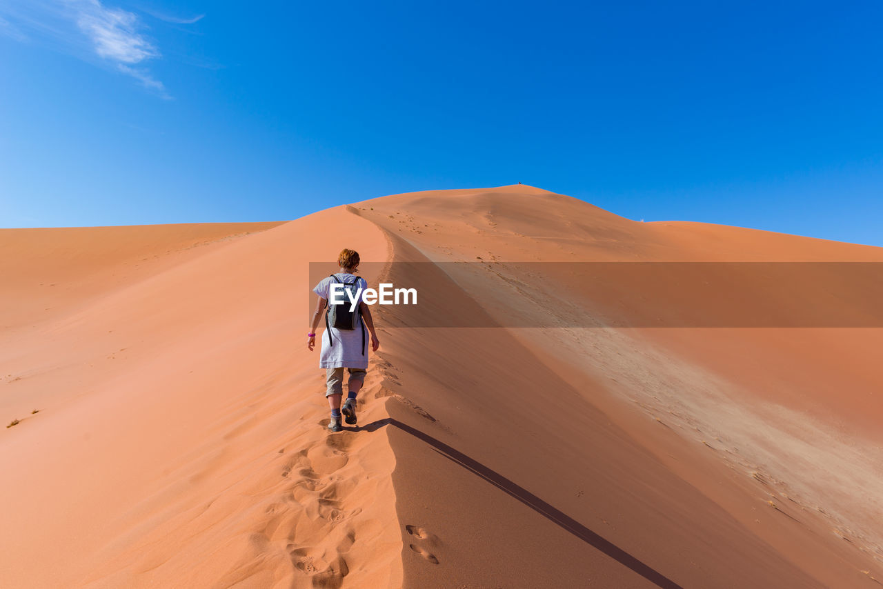 Rear view of man in desert against blue sky