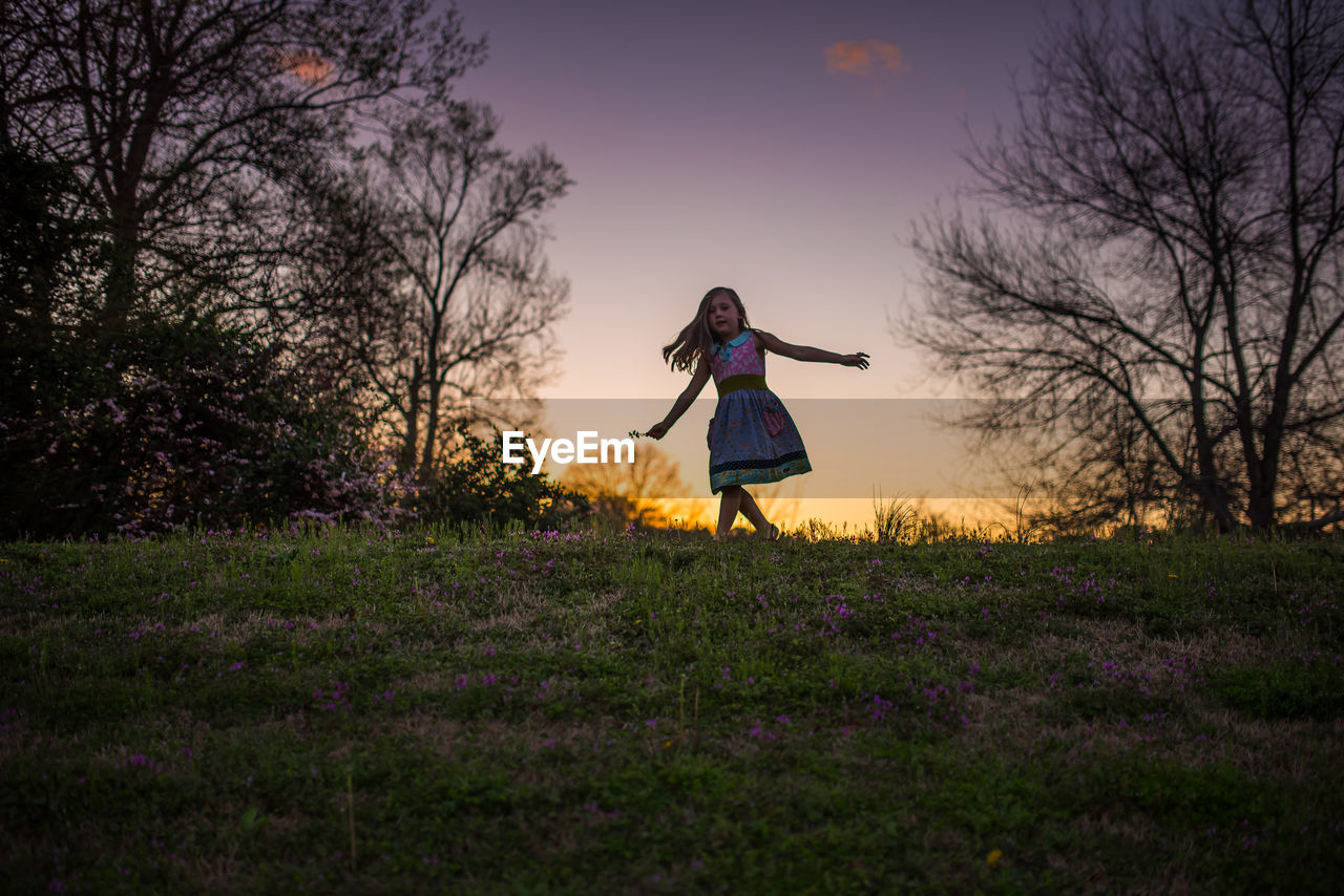 Little girl dancing sunset grass flowers silohette hill trees twirling