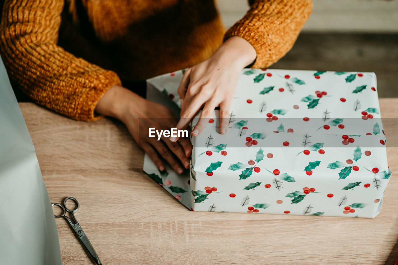 Midsection of woman wrapping christmas gift by table