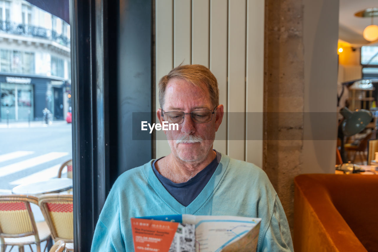 Age, tourism, travel and people concept - senior with map and city guide of paris, sitting in cafe.