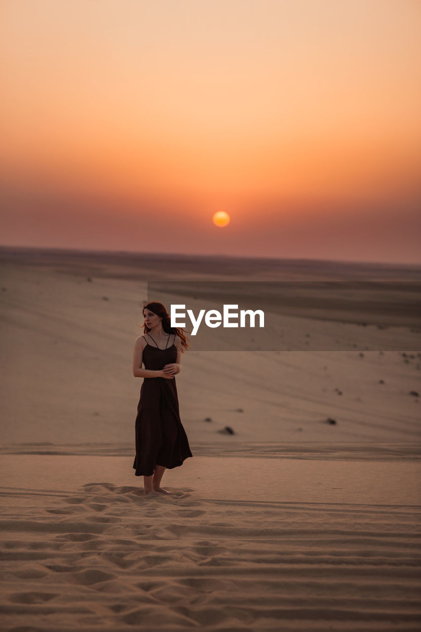 Woman in black dress strolling on sand while spending time in desert in sunrise in doha, qatar