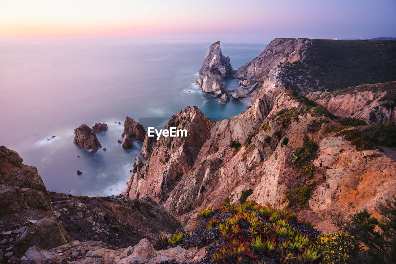 Panoramic view of rocks and sea against sky during sunset