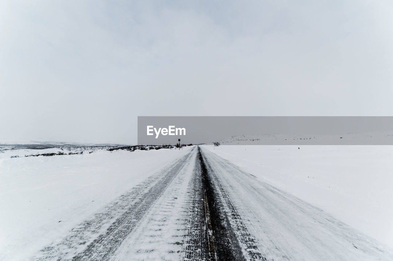 SNOW COVERED ROAD AGAINST SKY DURING WINTER