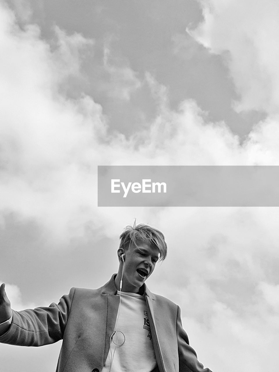 Low angle view of man with headphones against cloudy sky