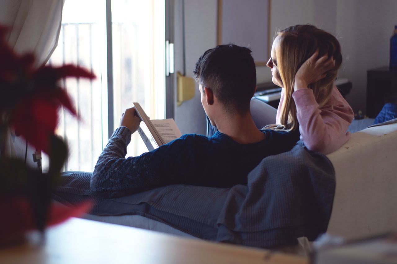 Couple reading book while sitting on sofa at home