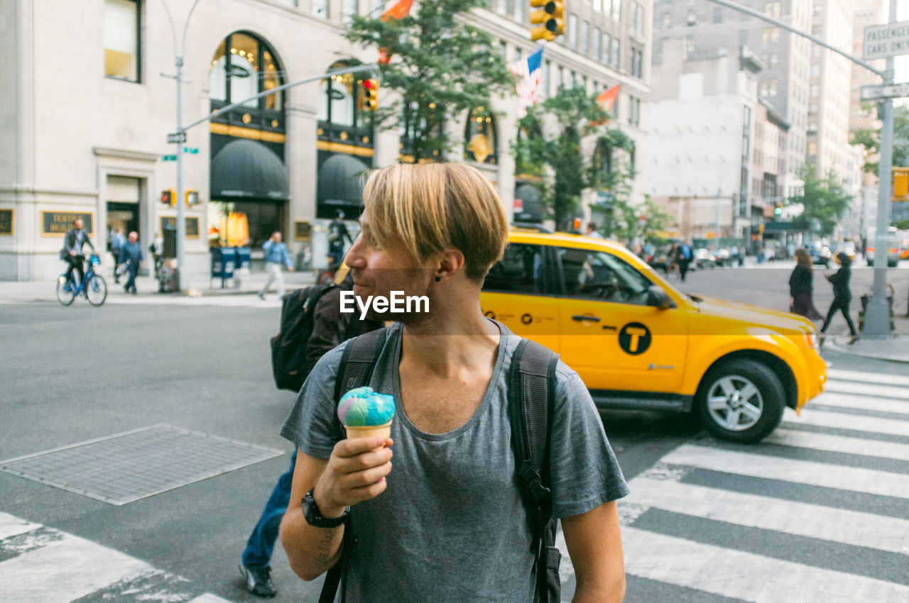 Smiling young man holding ice cream while looking away in city