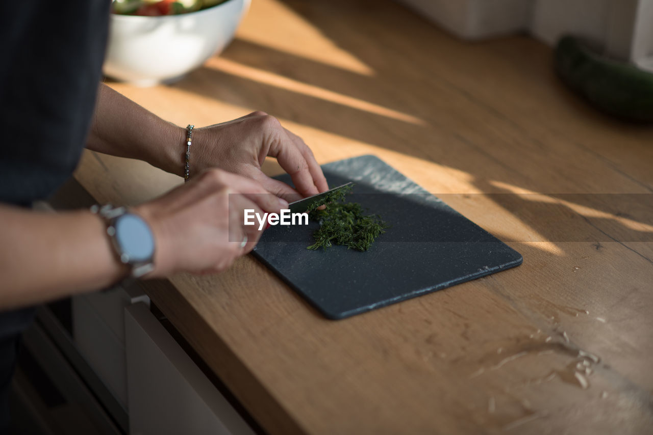 adult, one person, indoors, hand, food and drink, food, kitchen, lifestyles, women, table, domestic life, domestic kitchen, selective focus, occupation, domestic room, plant, healthy eating, wood, home interior, wellbeing, preparing food, high angle view, freshness, home, vegetable, holding, green, men, skill, cutting board, working, business, day, flooring, creativity, young adult, nature, female