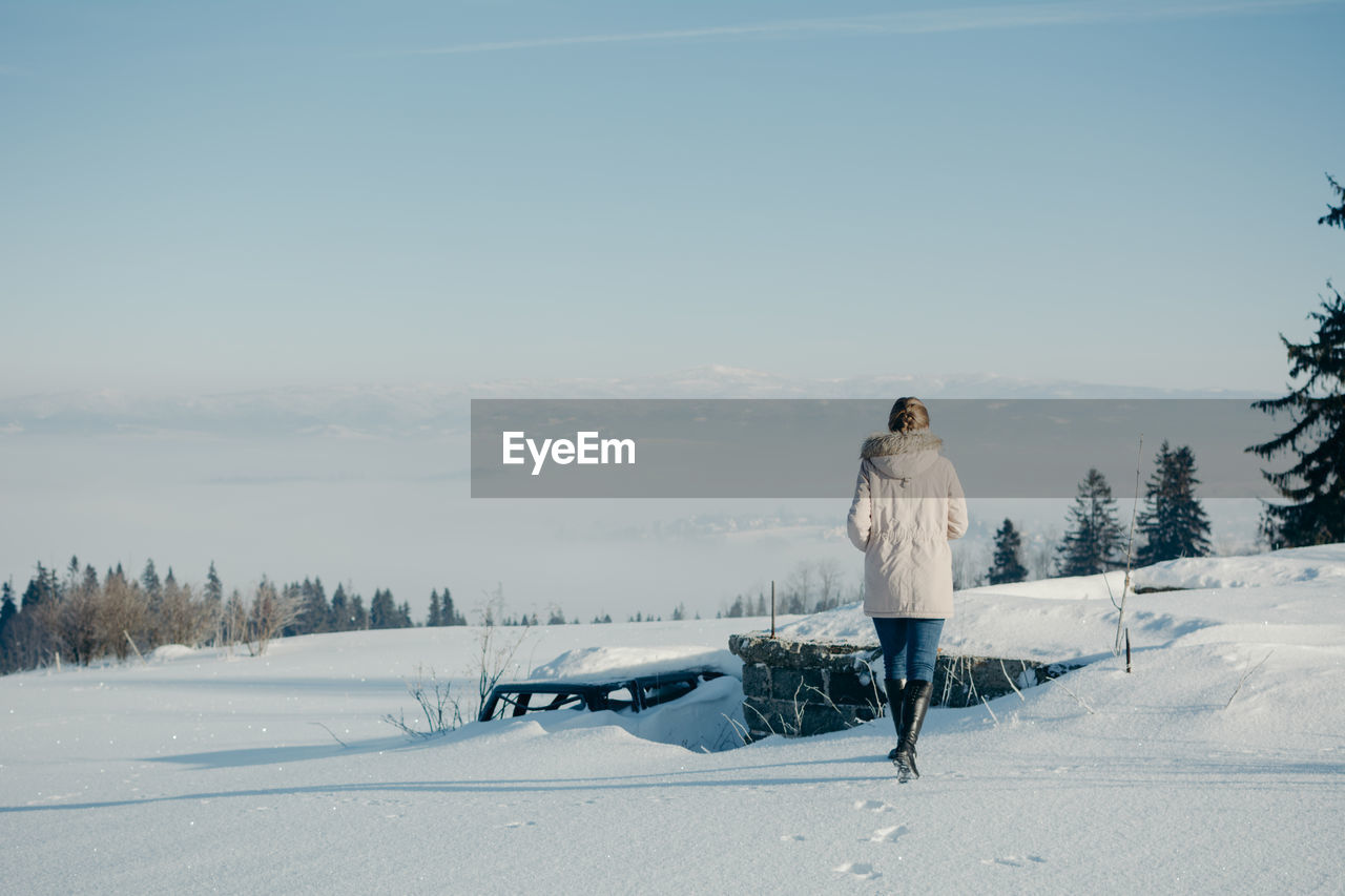 Rear view of woman walking on snow covered land against sky during winter