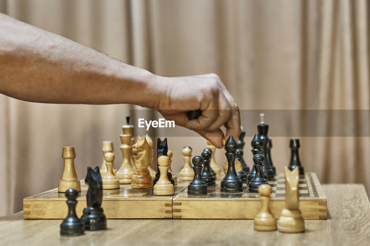 Old chess pieces on board. hand of mature man making move with white pawn by capturing  black piece.