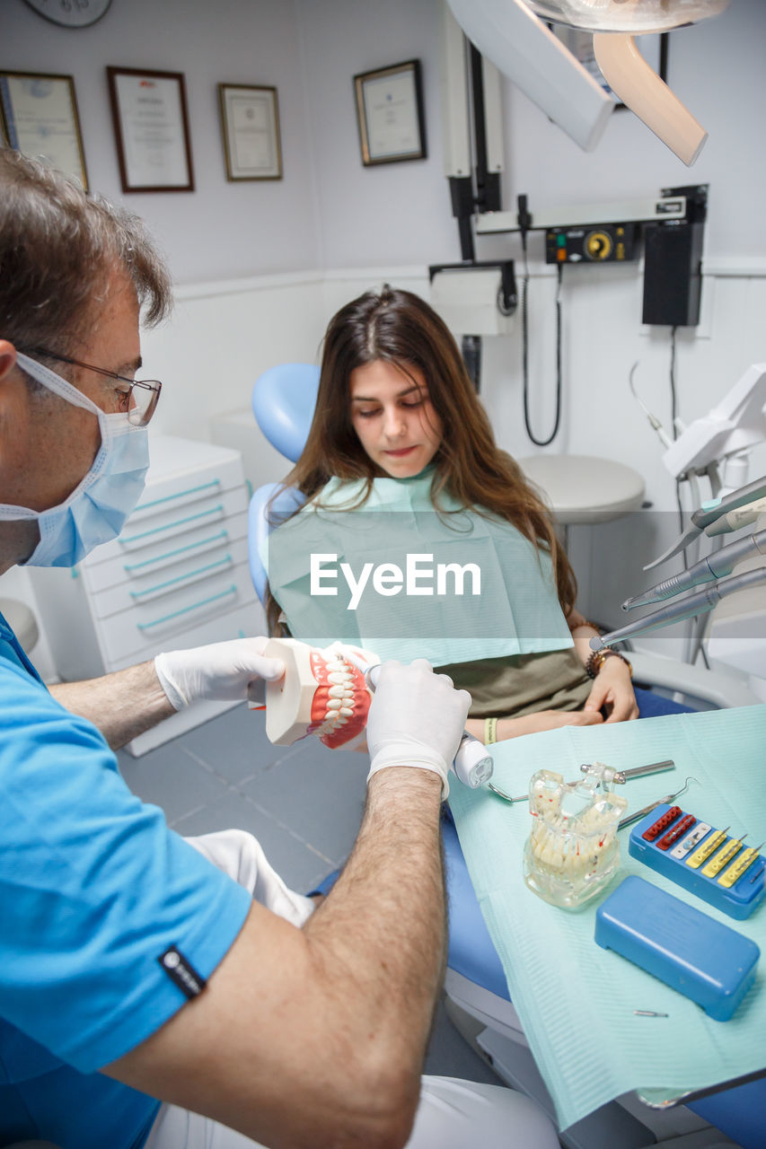 Professional doctor demonstration process of healthy teeth brushing to young woman sitting in chair.