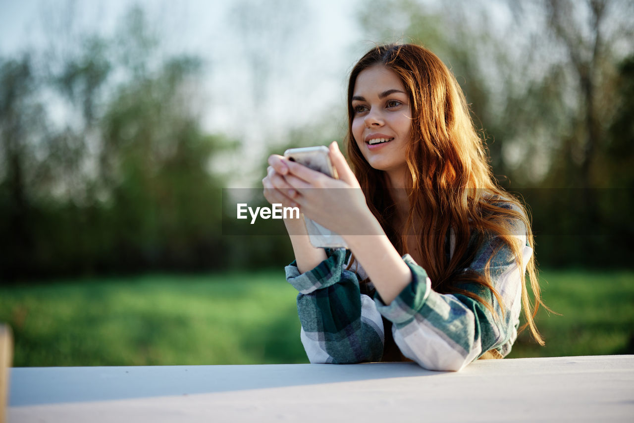 young woman using phone while sitting on table