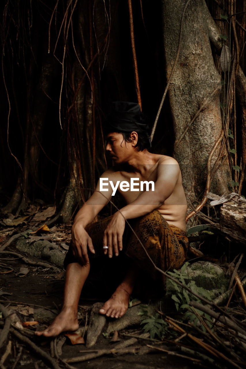 Low angle view of shirtless man sitting in forest