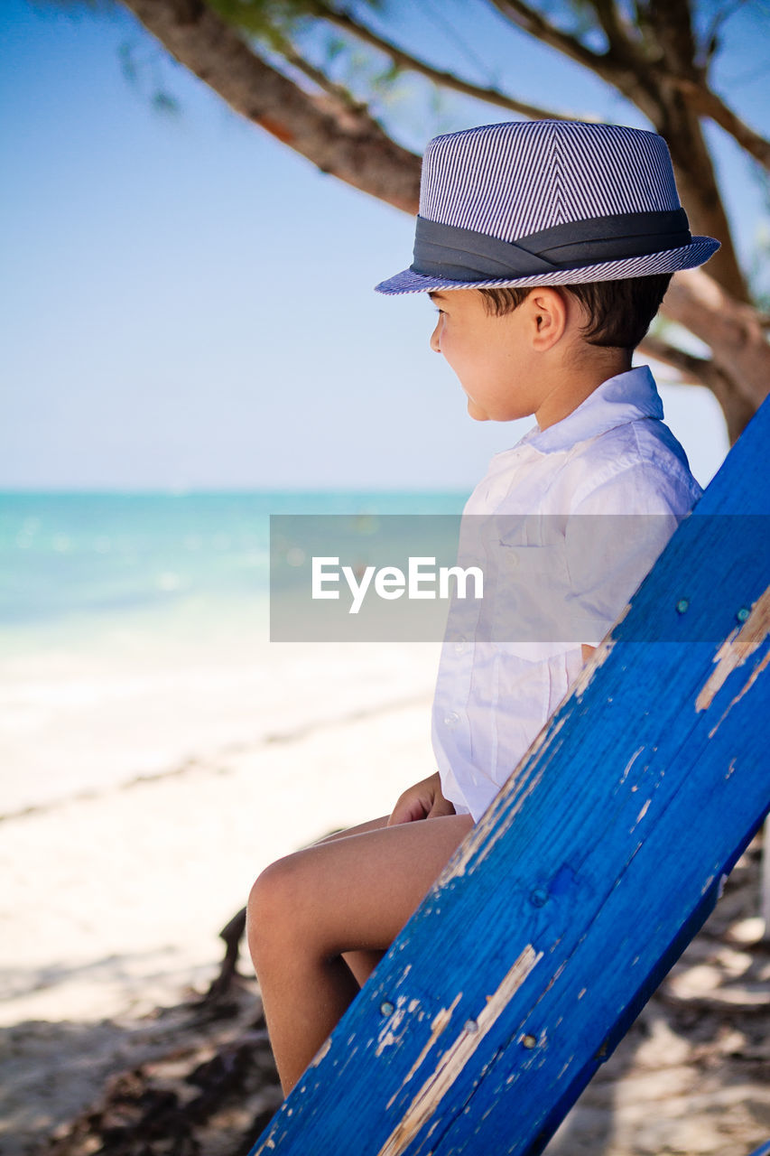 Little boy sitting on ladder at the beach watching caribbean waters