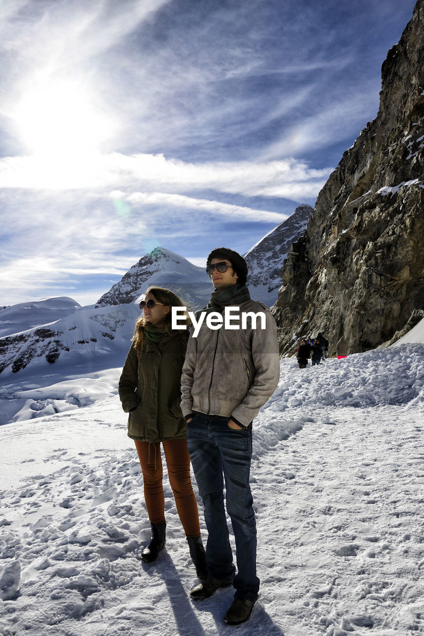 FRIENDS STANDING ON SNOW COVERED MOUNTAINS