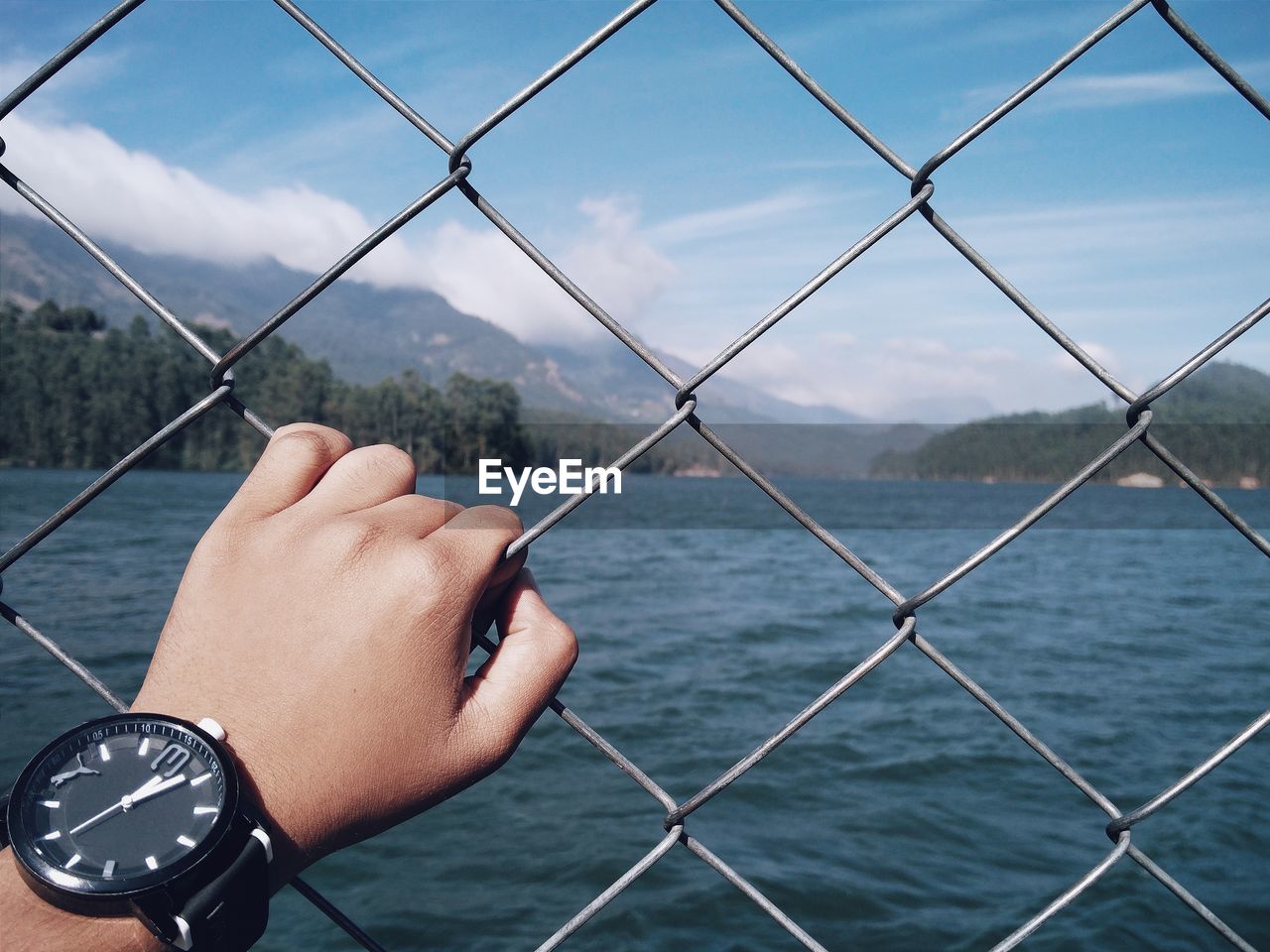 Cropped hand holding chainlink fence against river