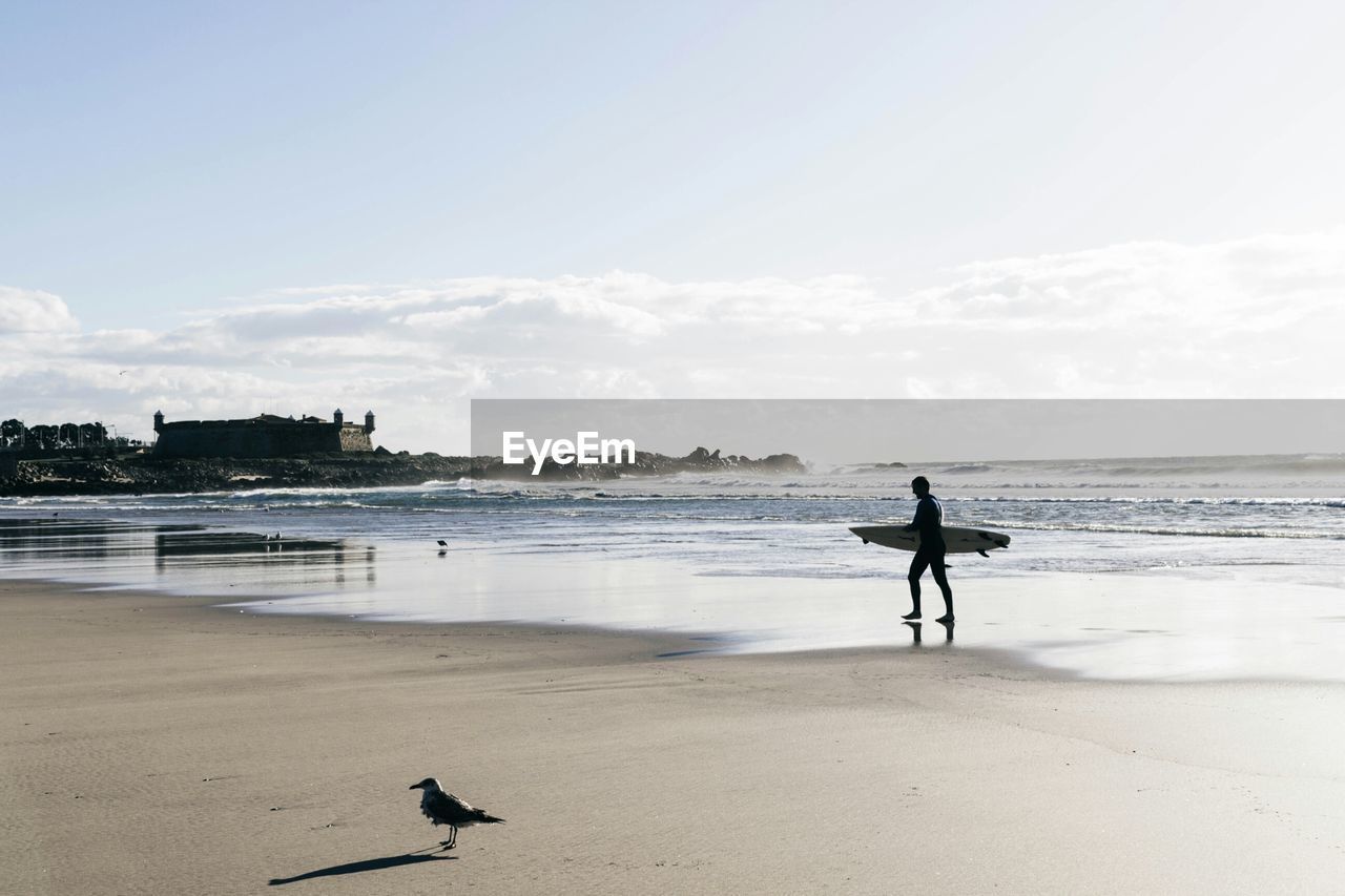 Full length of man with surfboard at beach against sky