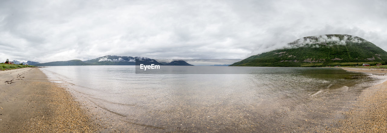 Panoramic view of sea by mountains against cloudy sky