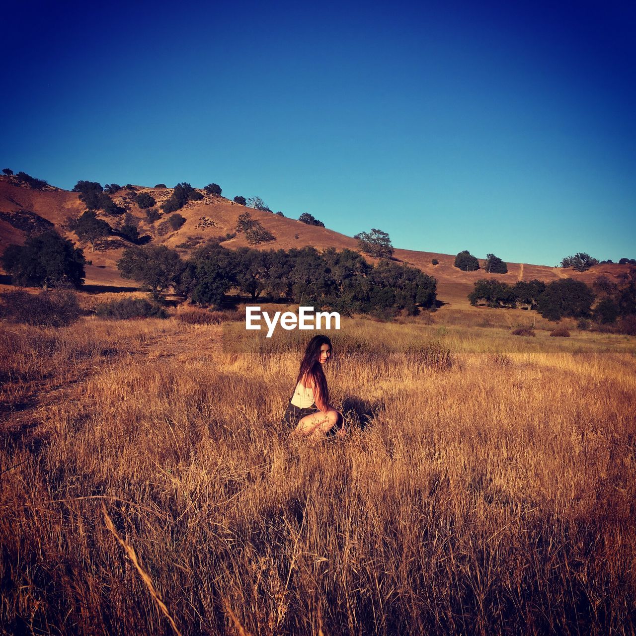 Woman crouching at grassy field against clear blue sky