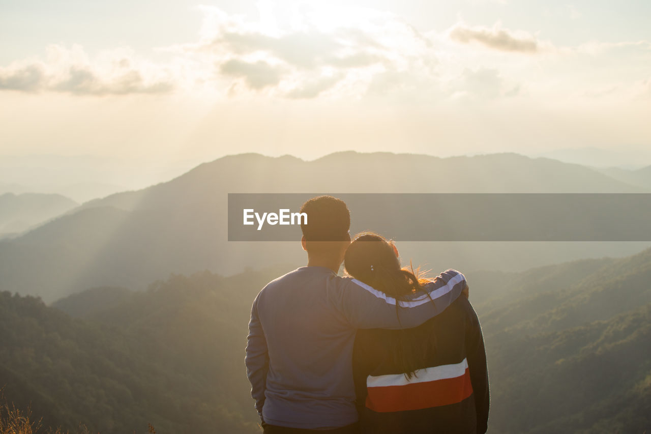 Rear view of couple looking at mountains against cloudy sky