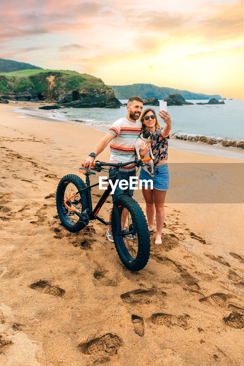 Couple with fat bike taking a selfie with their dog on the beach