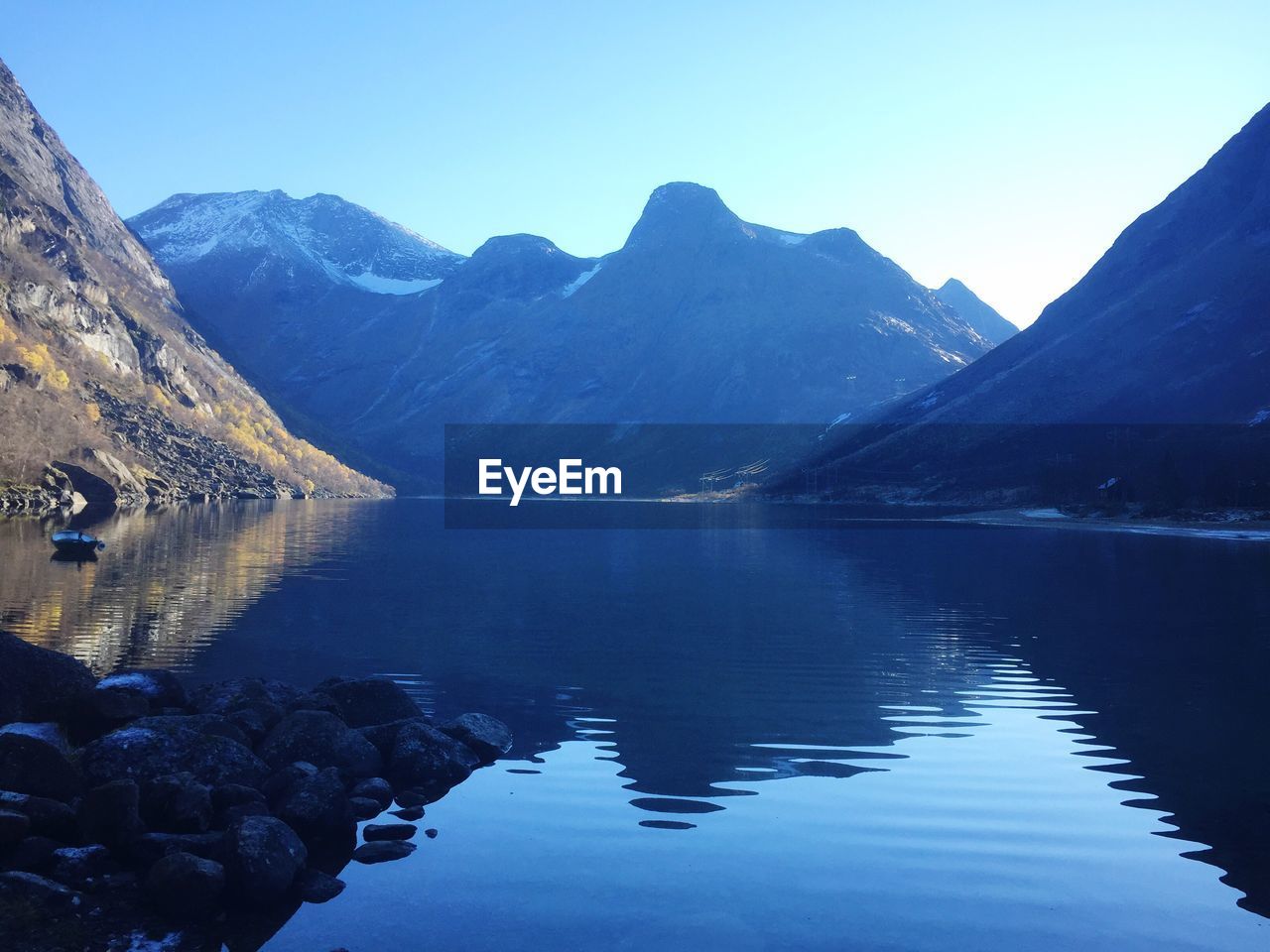 Scenic view of calm lake surrounded by mountains against clear blue sky