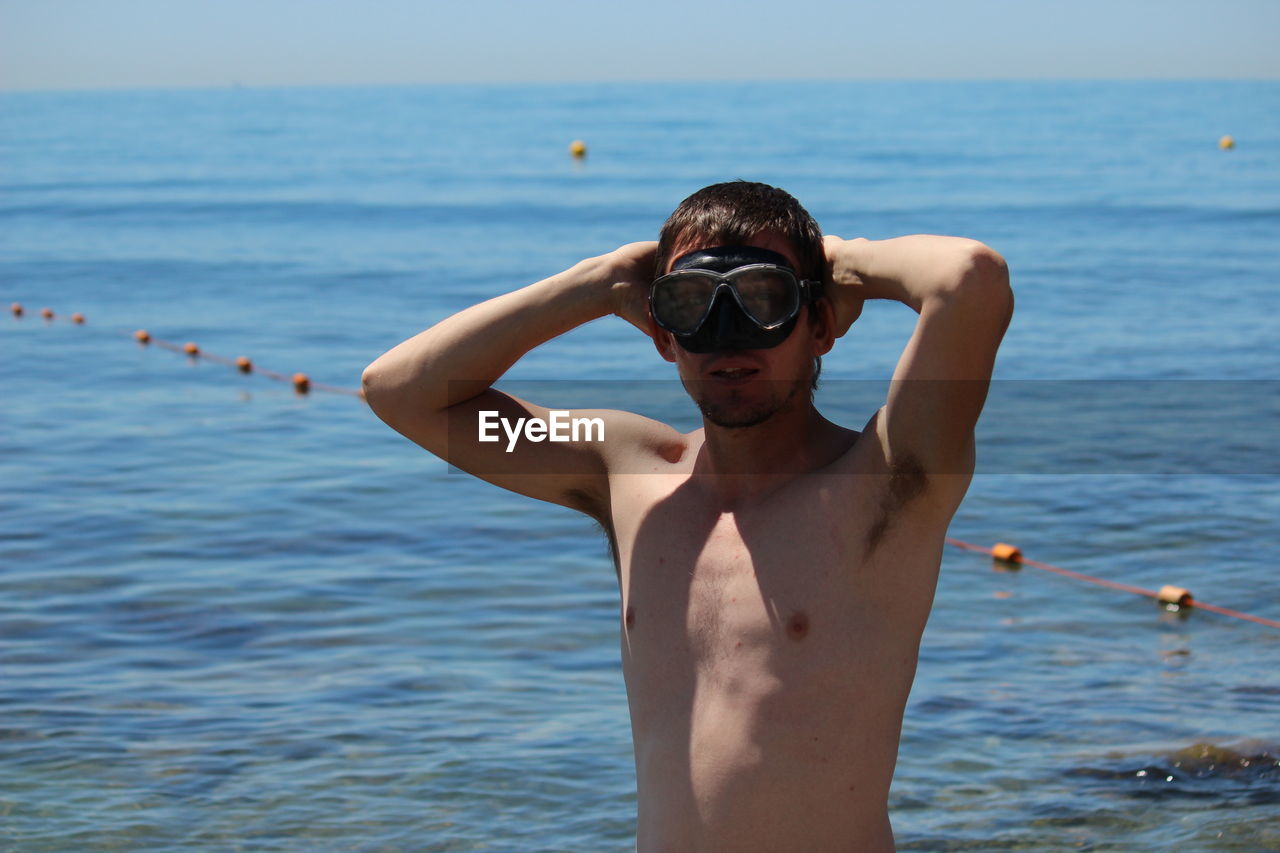 Portrait of shirtless man standing in sea against sky