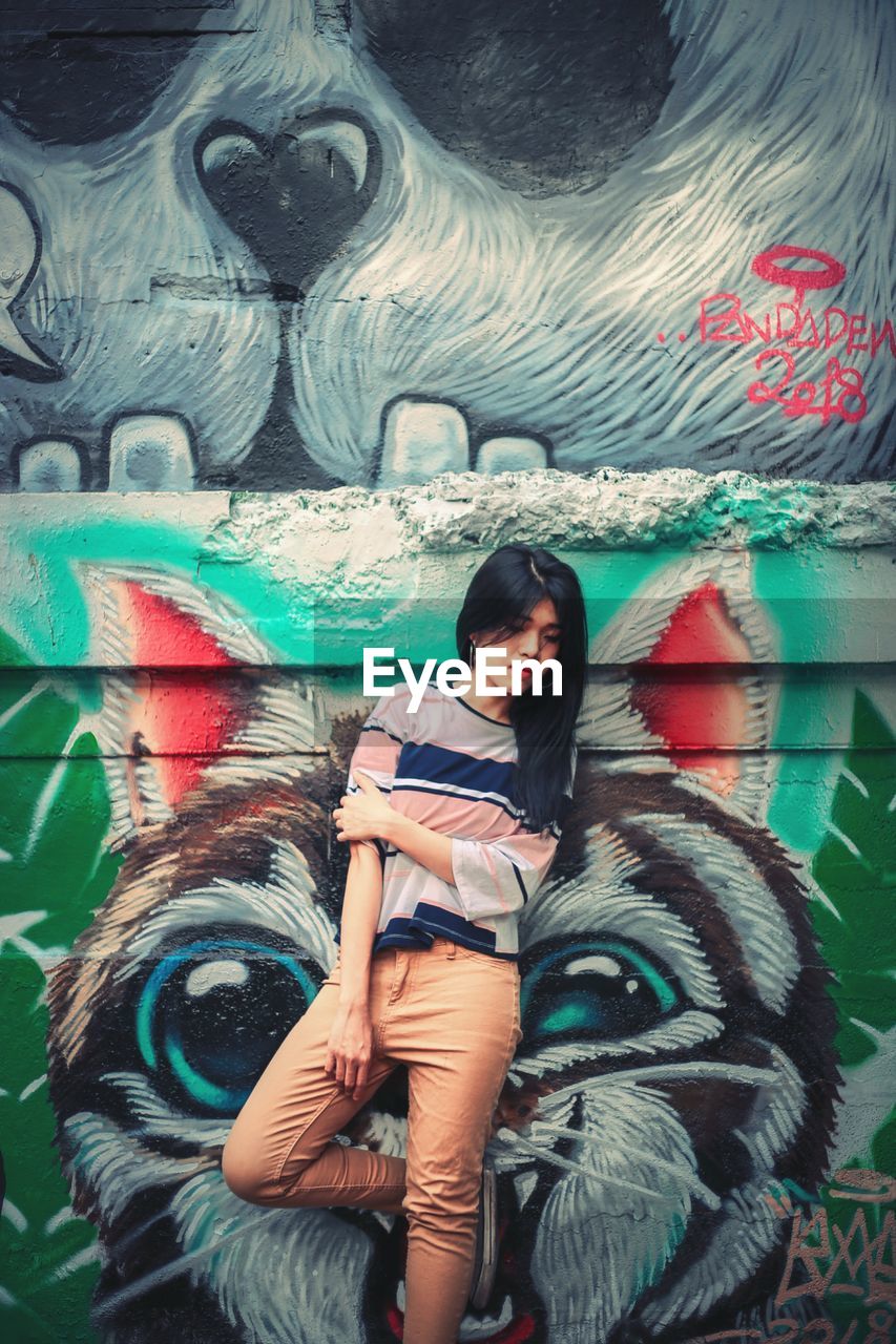 Young woman looking down while standing against wall