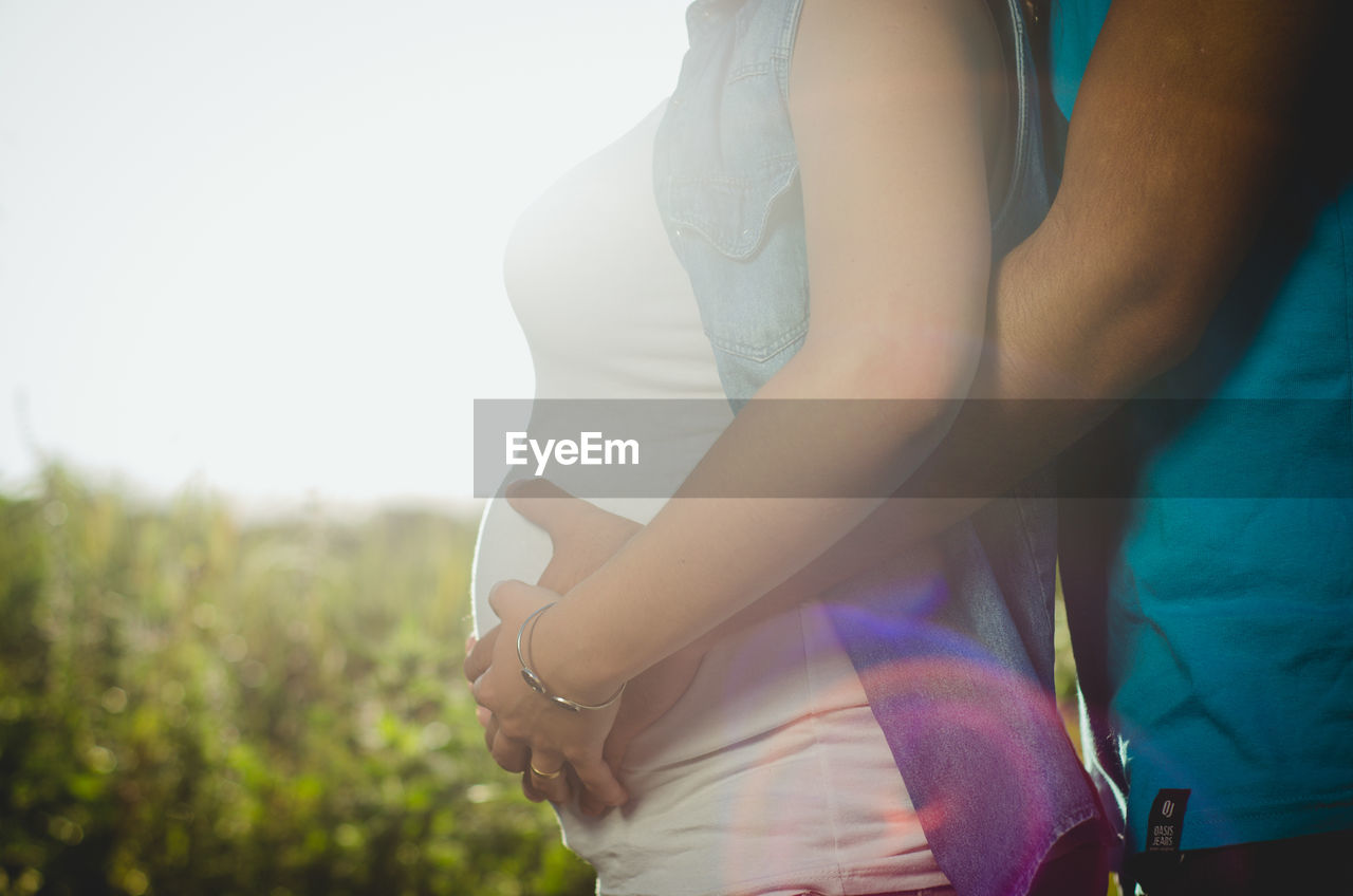 Midsection of man embracing pregnant woman while touching abdomen