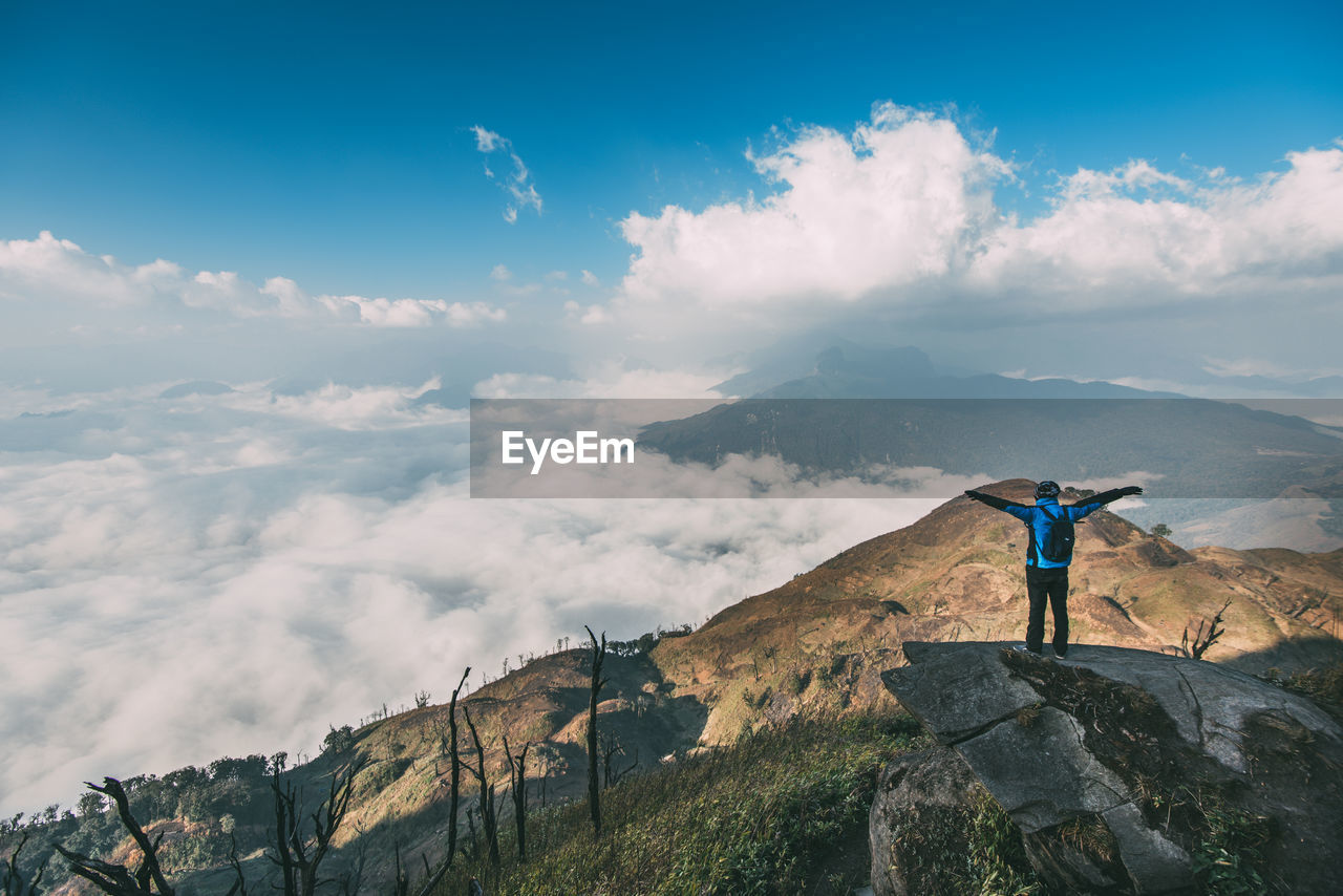 Woman standing on rock looking at mountain against sky