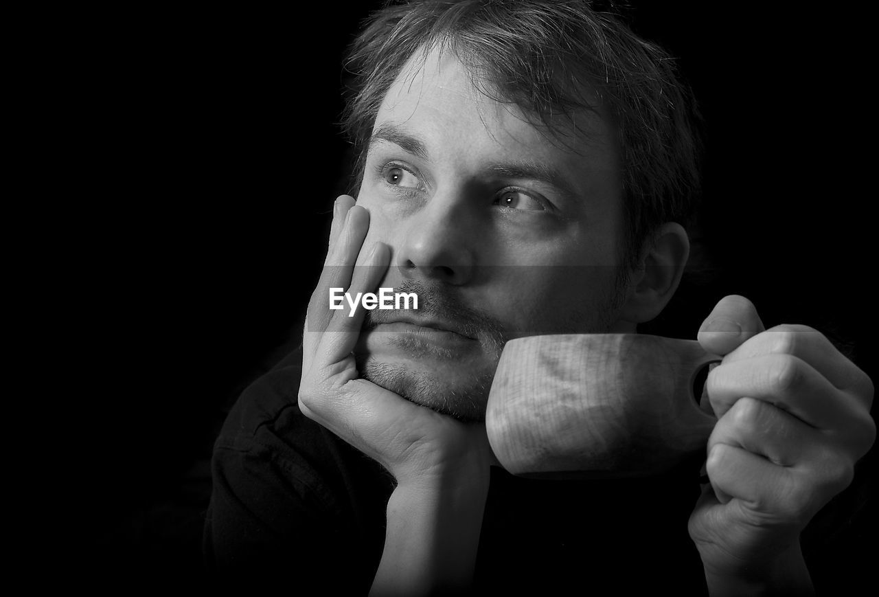 Close-up of thoughtful man having coffee against black background