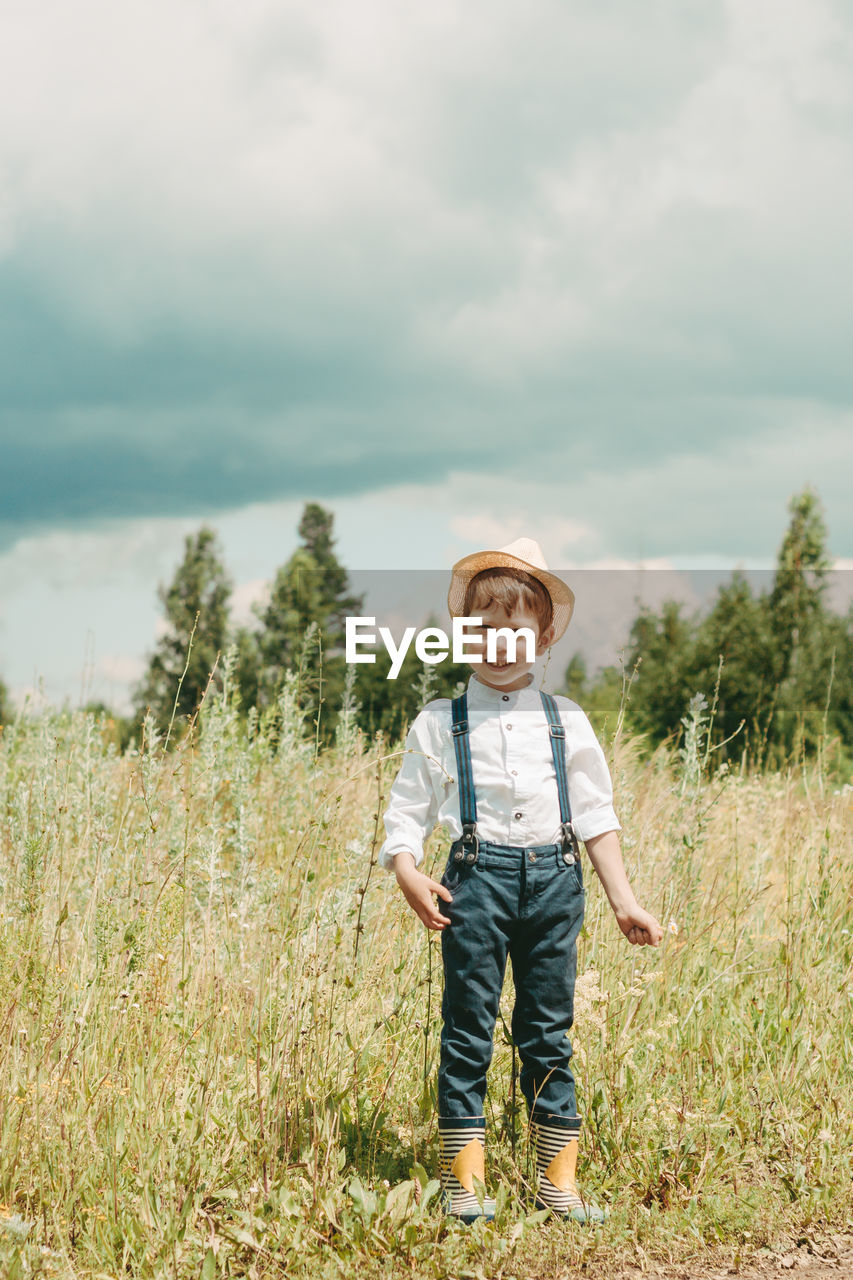 Little farmer on a summer field, cute little boy in a straw hat. boy with a flower stands 