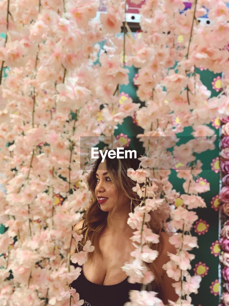 Smiling woman standing amidst pink flowers while looking away