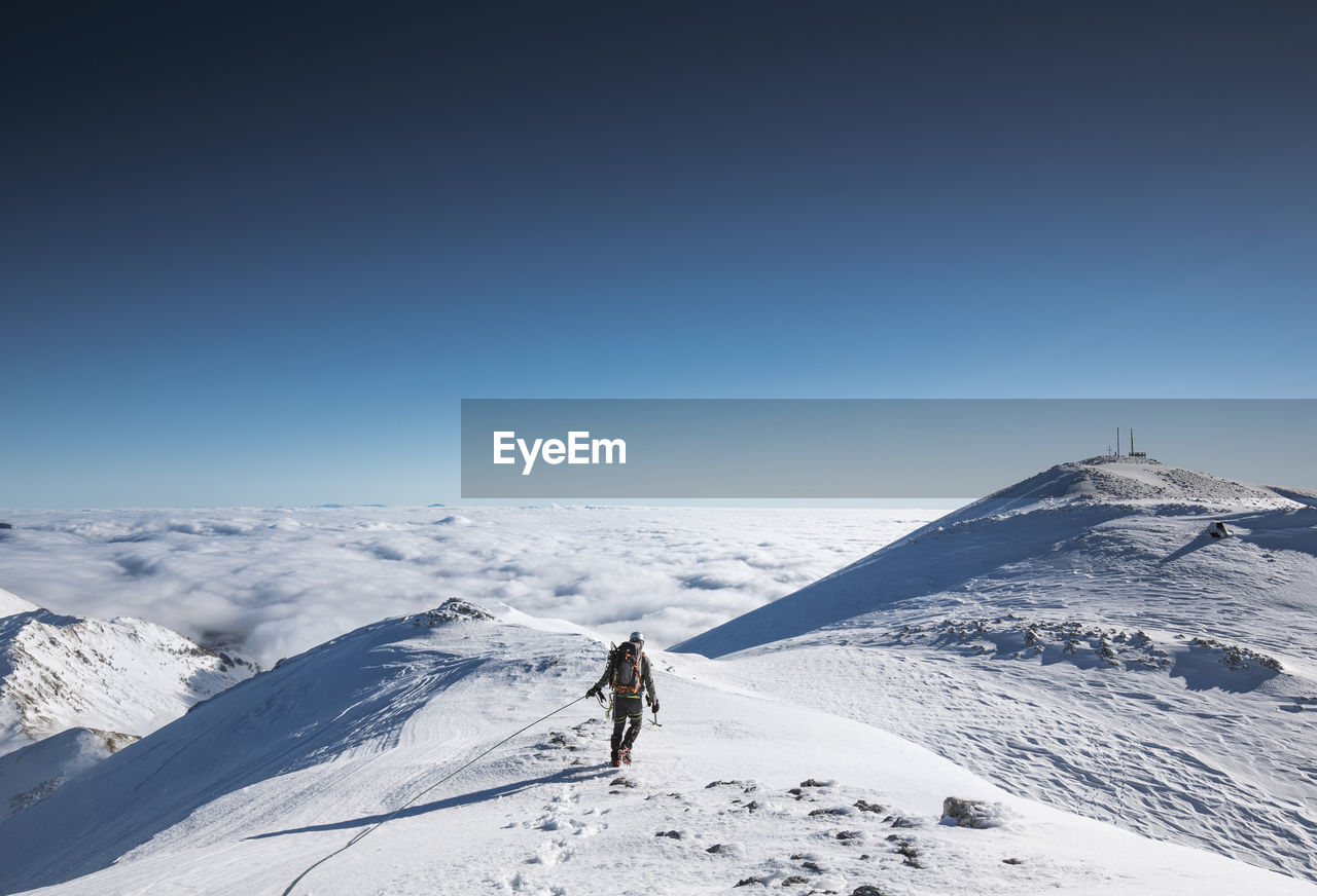 Man walking on snowcapped mountain against blue sky