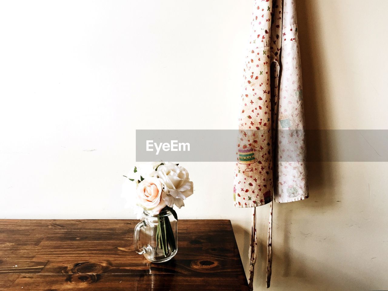 Roses blooming in glass container on wooden table against wall