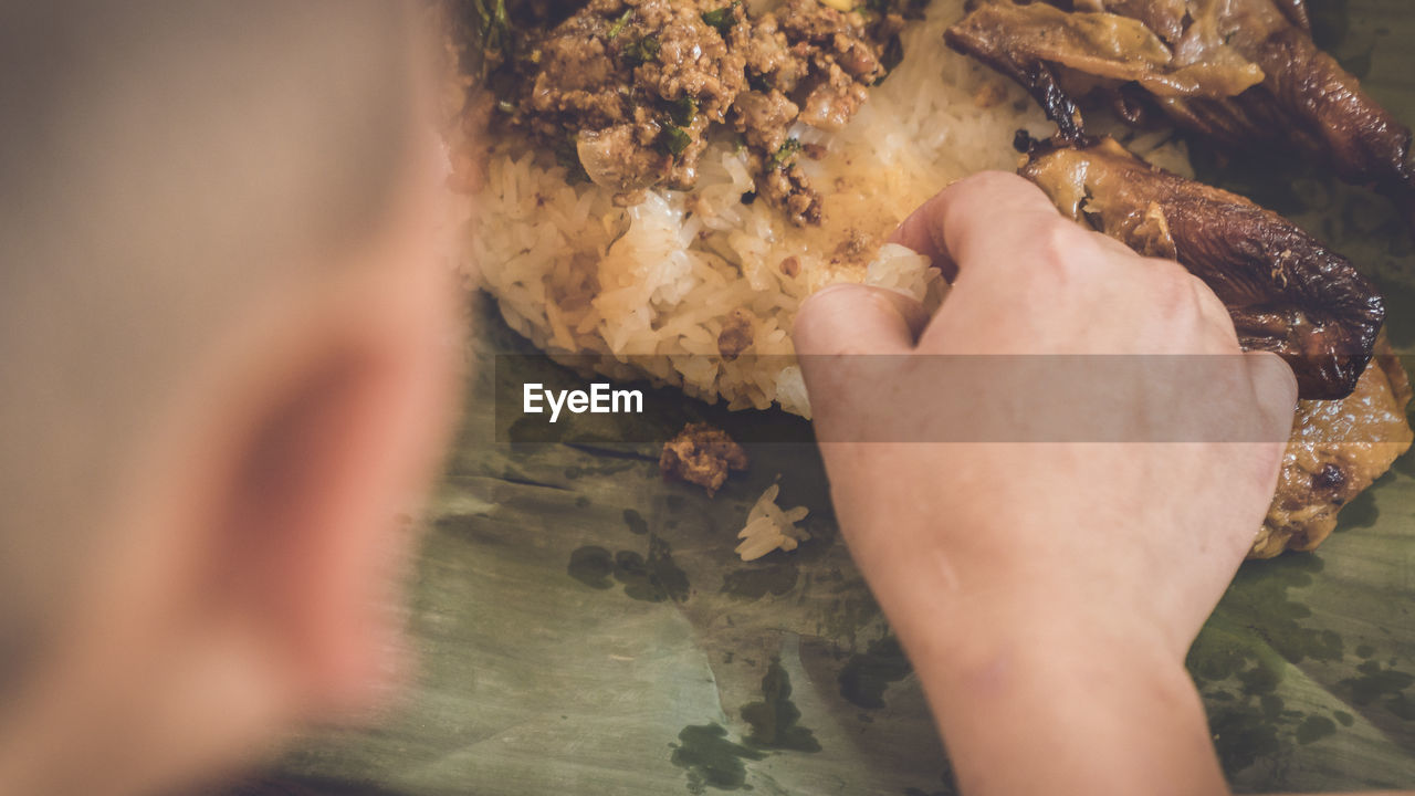 Close-up of person hand eating food in banana leaf