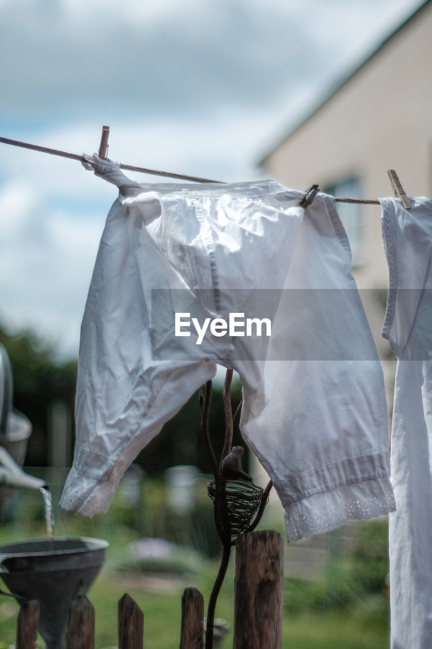 CLOSE-UP OF CLOTHES DRYING ON CLOTHESLINE AGAINST WALL