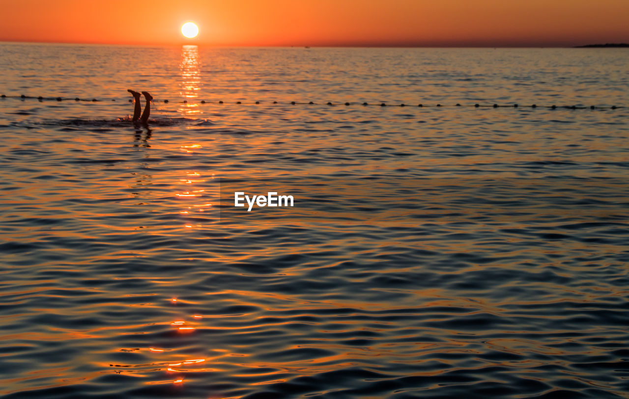 Silhouette person standing in sea against sky during sunset