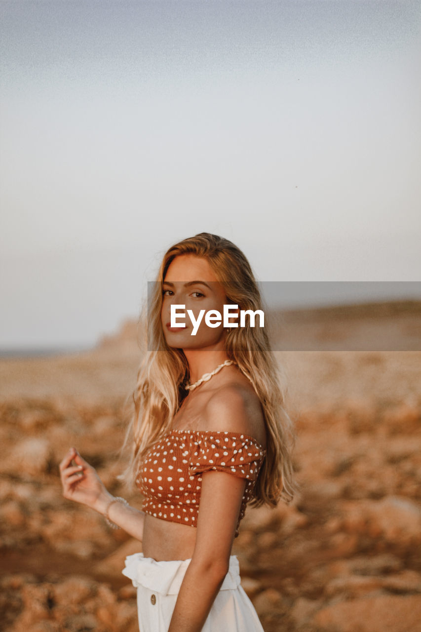 Portrait of beautiful woman standing at beach against sky