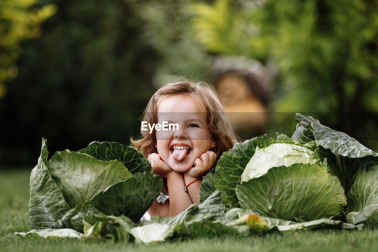 Portrait of cute smiling girl making face while lying on grass outdoors