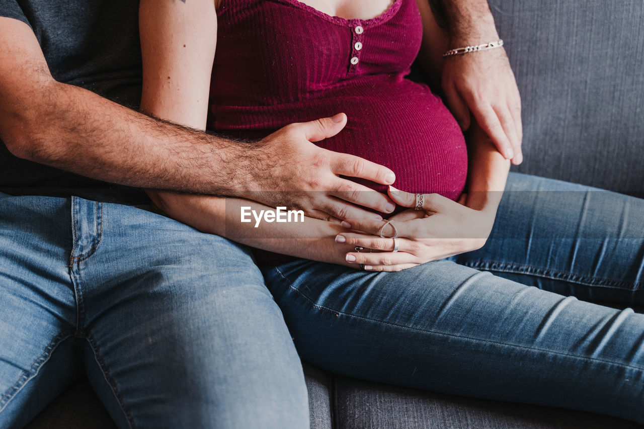 Midsection of pregnant woman sitting with male partner on sofa at home