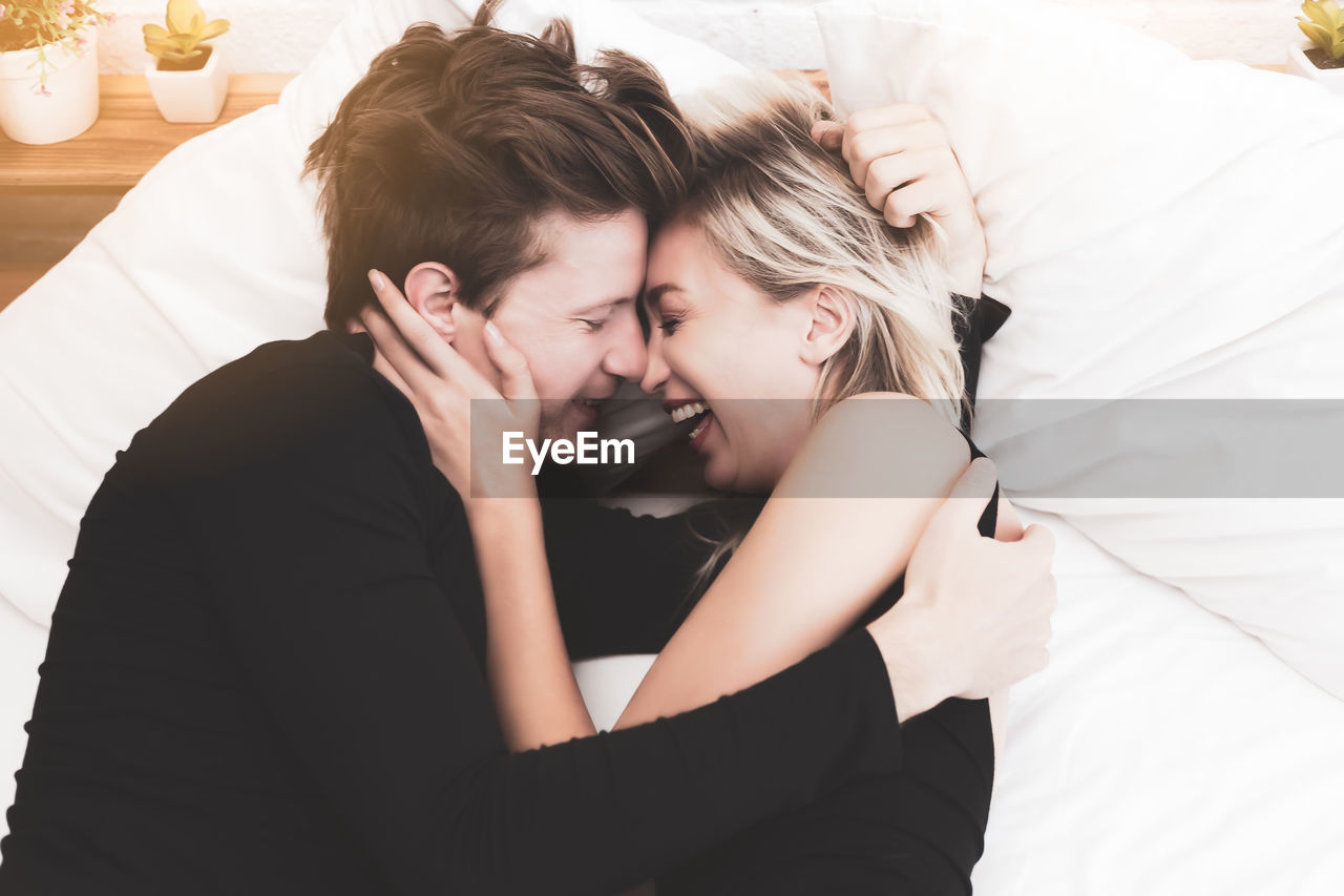 Directly above shot of cheerful couple lying face to face on bed