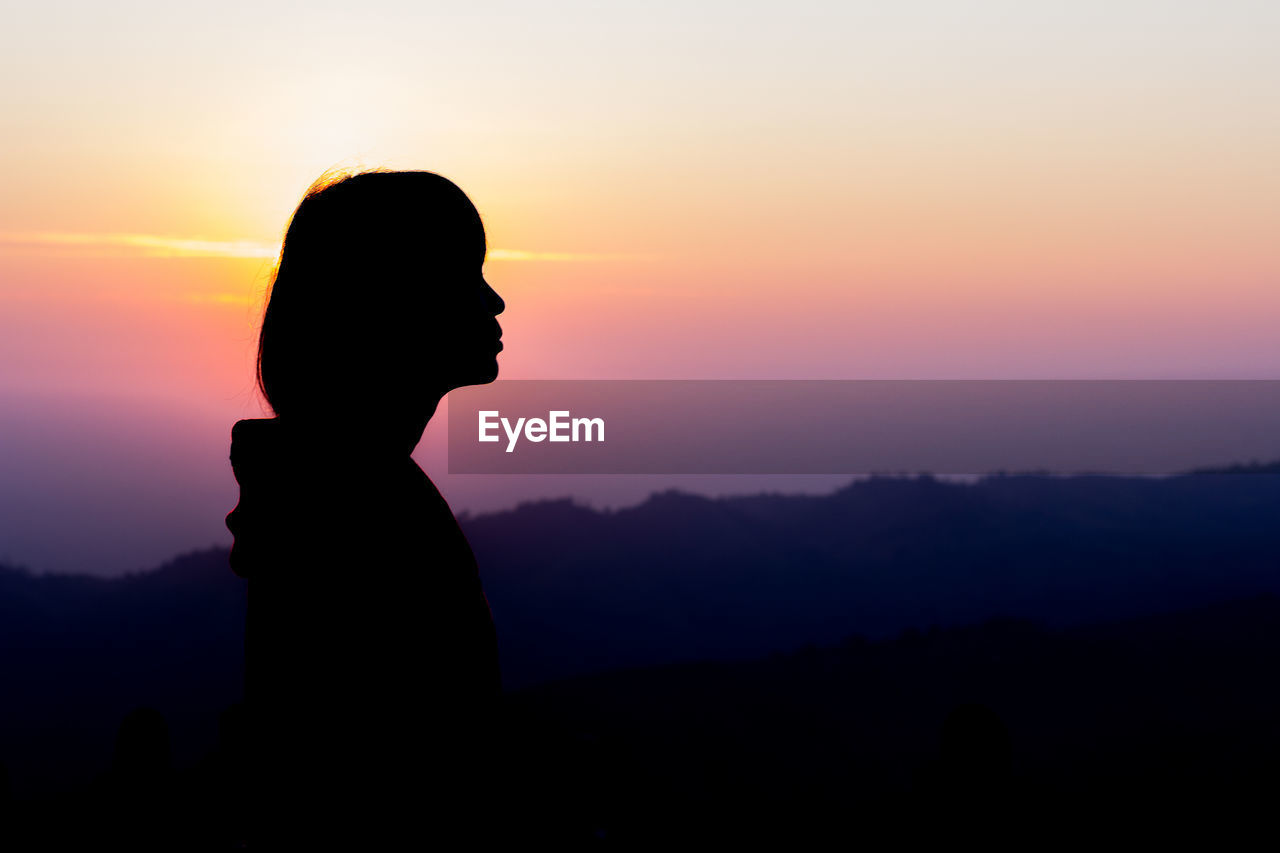 SILHOUETTE WOMAN STANDING AGAINST SKY AT SUNSET