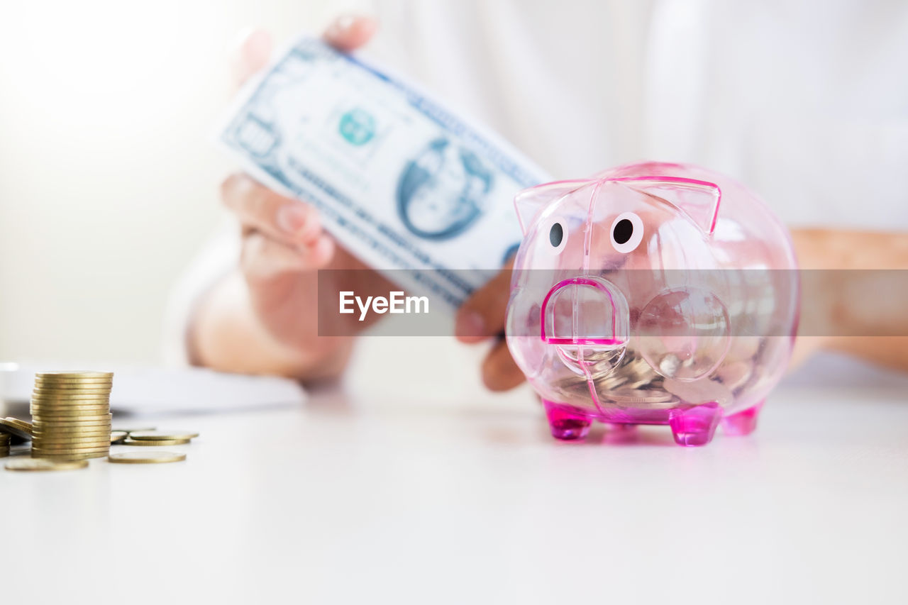 Midsection of man holding paper currency with piggy bank in foreground