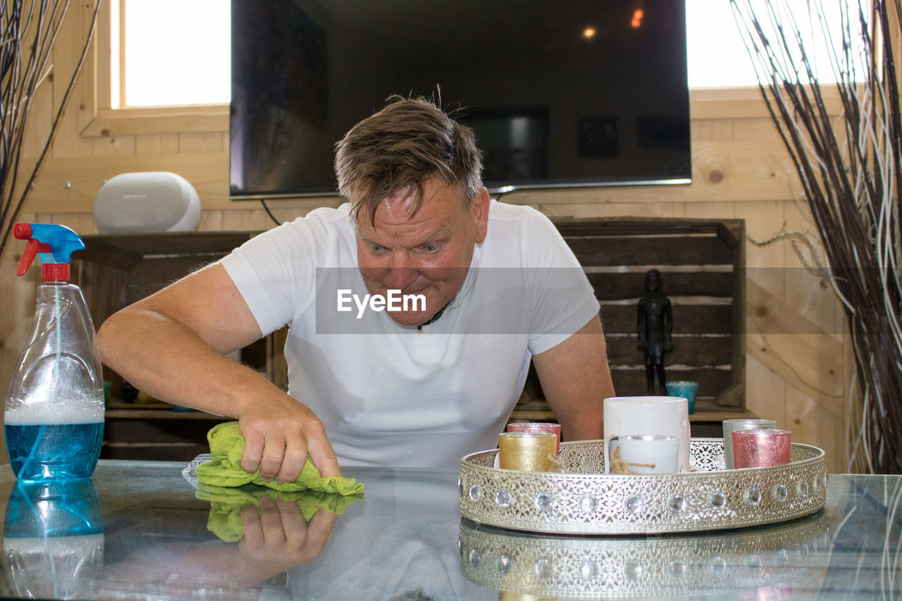 Mature man cleaning table at home