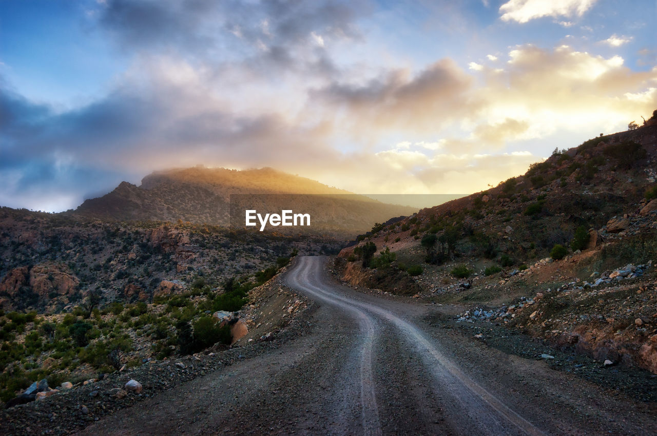 Road leading towards mountains against sky during sunset