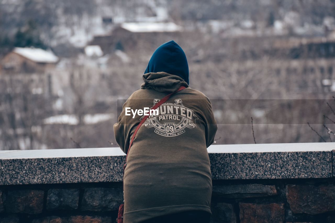 rear view, one person, winter, blue, cold temperature, clothing, architecture, adult, lifestyles, hood, snow, men, warm clothing, hood - clothing, nature, leisure activity, day, focus on foreground, waist up, hat, outdoors, built structure, standing, spring, black, person, city, wall, railing