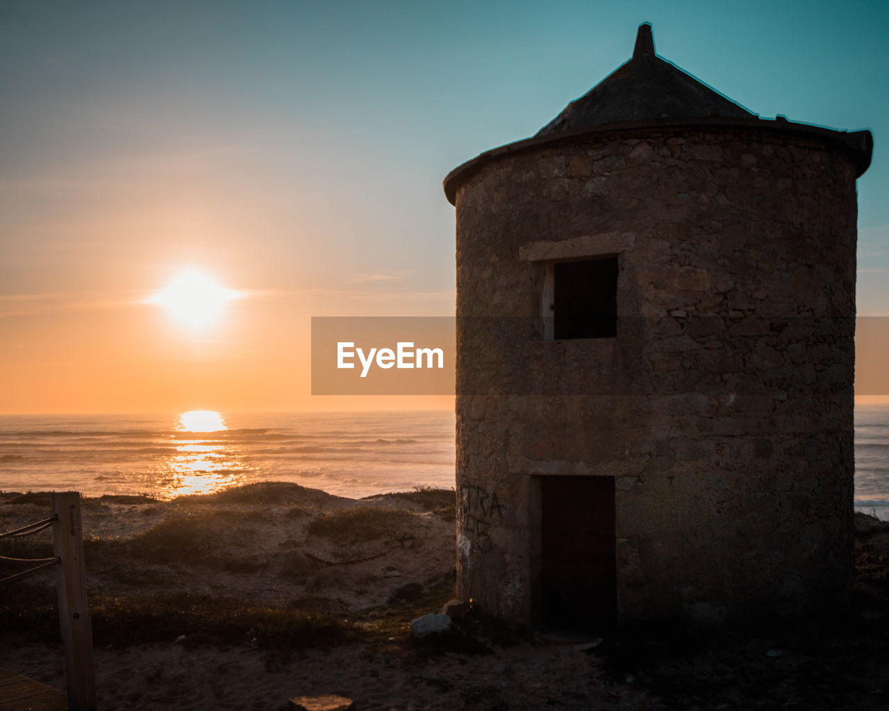 Built structure on beach by sea against sky during sunset