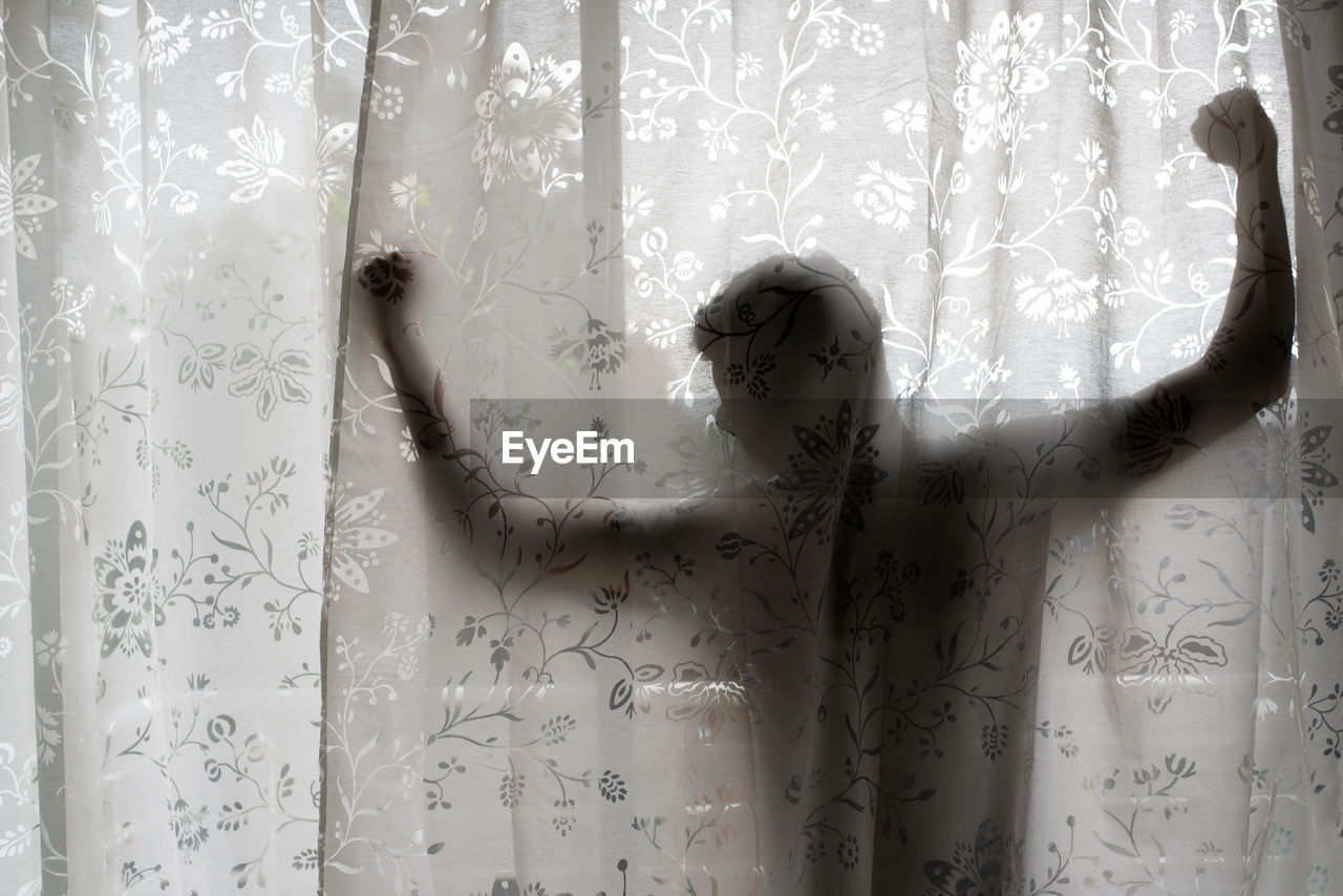 Man with arms outstretched standing in balcony seen through curtain