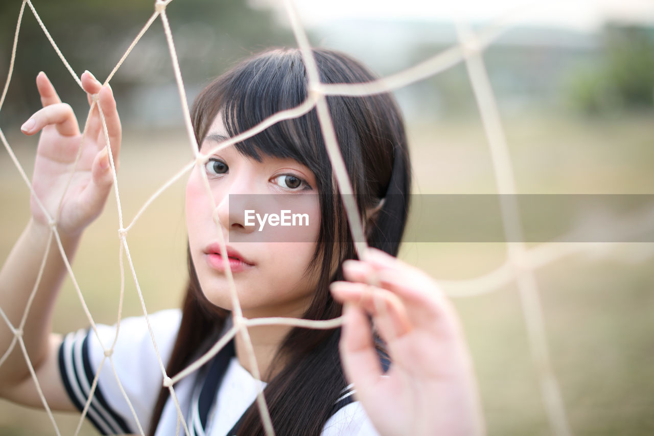 Portrait of young woman standing by sports net