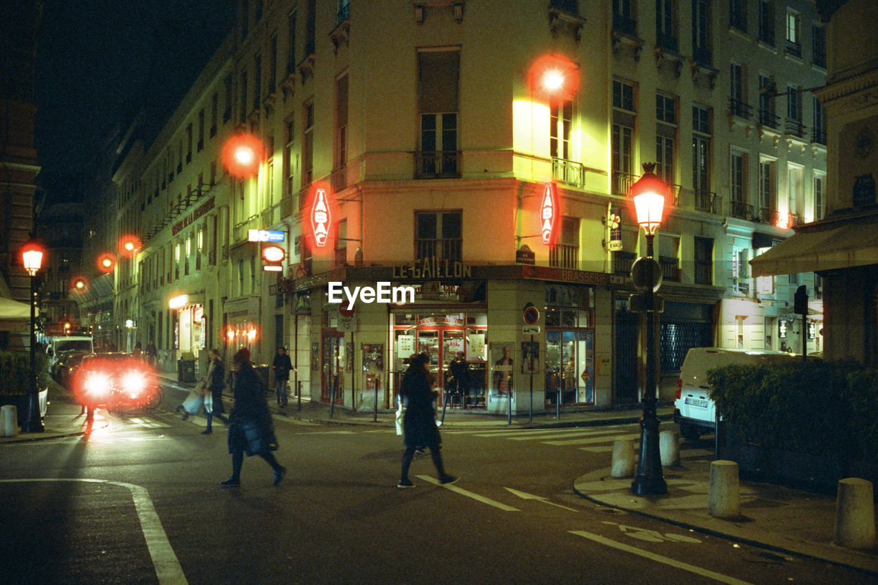 PEOPLE WALKING ON ILLUMINATED STREET AT NIGHT IN CITY